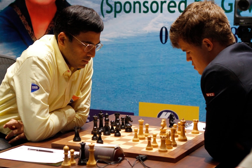 Two chess Grandmasters look down a the pieces on the board in front of them as they play in the World Chess Championship.