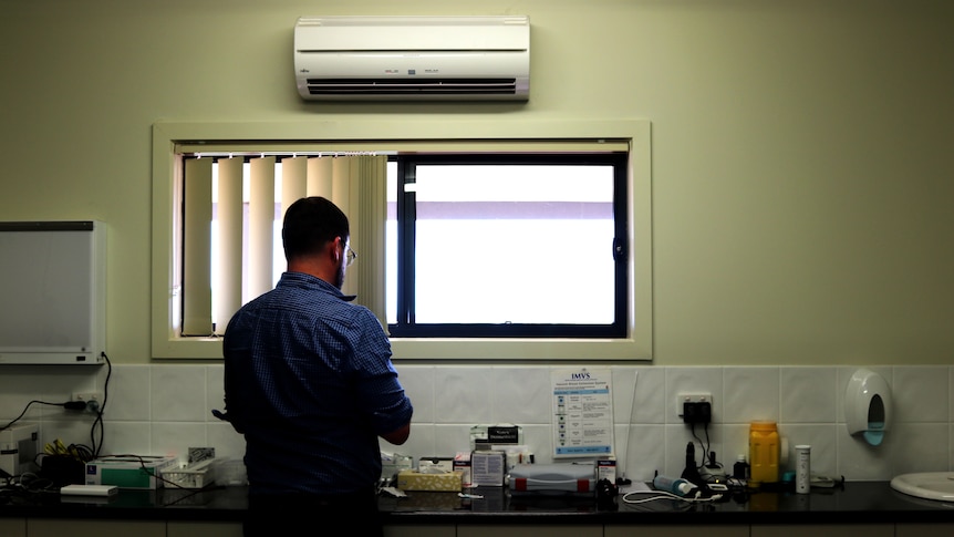 A doctor stands with his back to the camera, preparing to perform and injection.