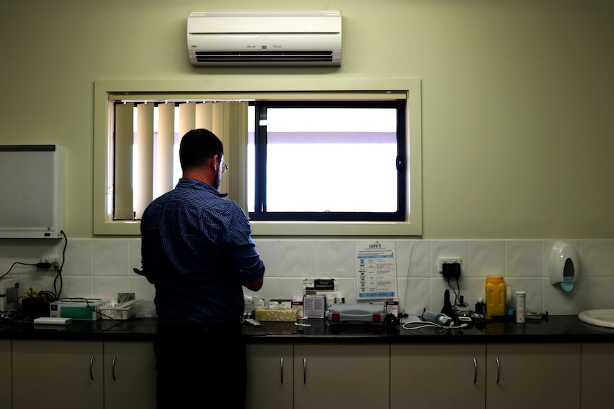 A doctor stands with his back to the camera, preparing to perform an injection.