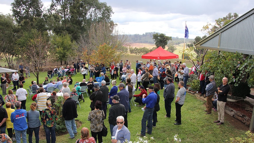 A crowd of people stand at a morning tea event on a rural property.