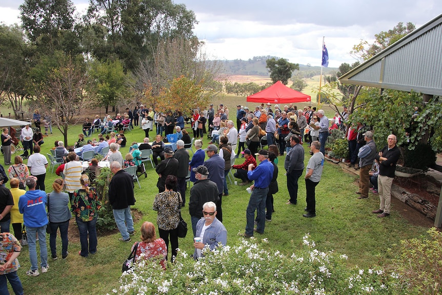 A crowd of people stand at a morning tea event on a rural property.