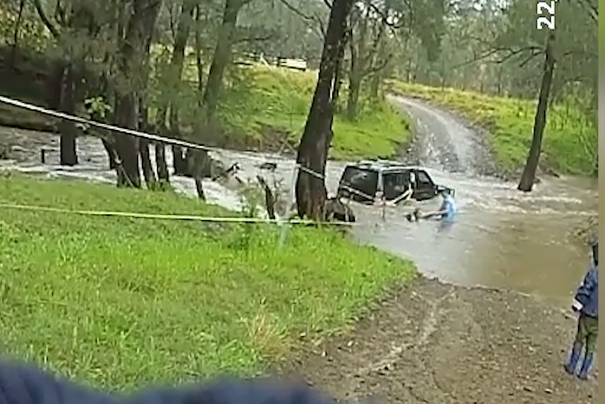 A police officer next to a submerged car pulling a woman through the water