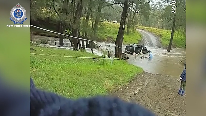 A police officer next to a submerged car pulling a woman through the water