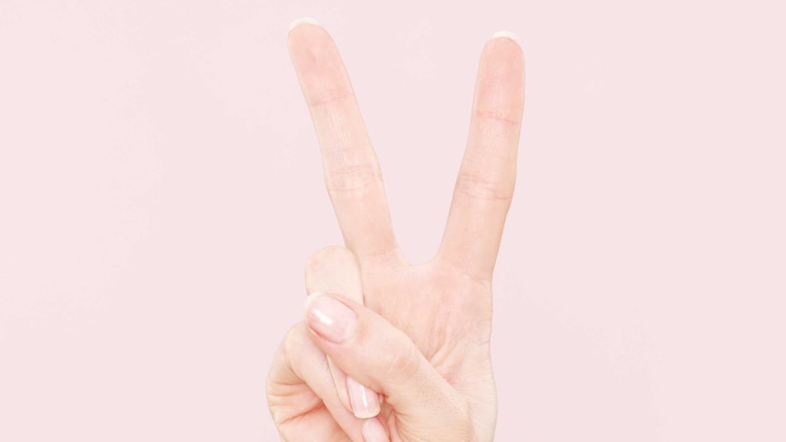 Woman's hand holds peace sign in front of pink background.