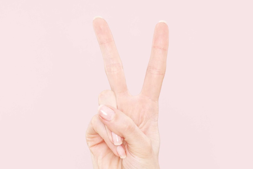 Woman's hand holds peace sign in front of pink background.