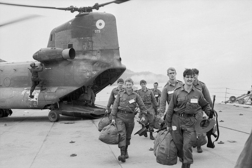 Soldiers walk from a helicopter on the deck of a ship.