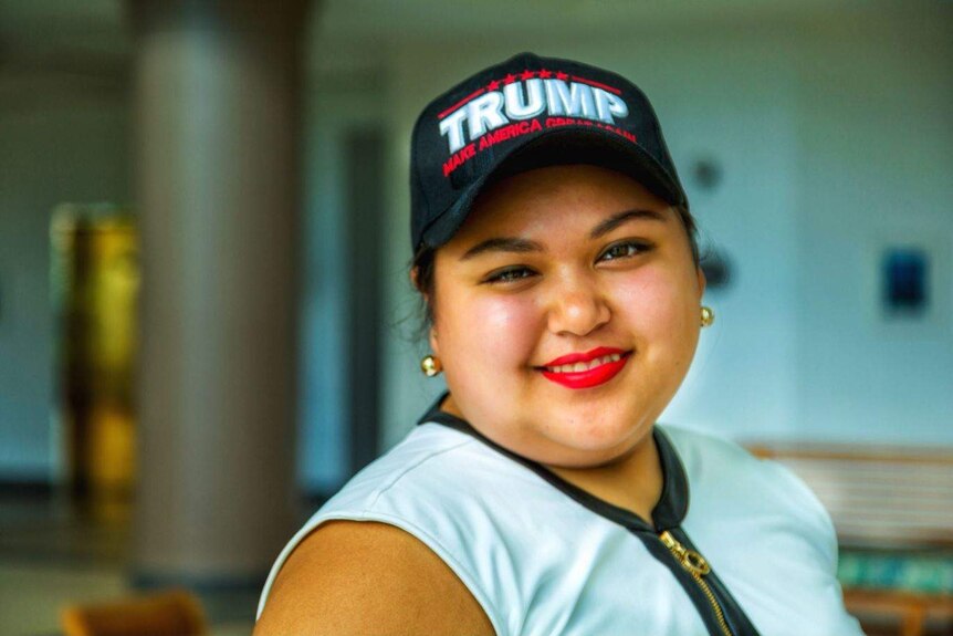 A close-up of a woman smiling at the camera wearing a "Trump: Make America Great Again" cap.