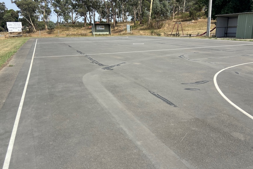 a photo of the netball court being patched up, showing cracks and rough surface 
