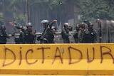 Venezuelan security forces throw tear gas grenades towards demonstrators behind graffiti that reads "dictator".