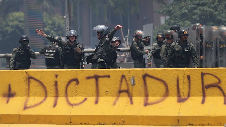 Venezuelan security forces throw tear gas grenades towards demonstrators behind graffiti that reads "dictator".