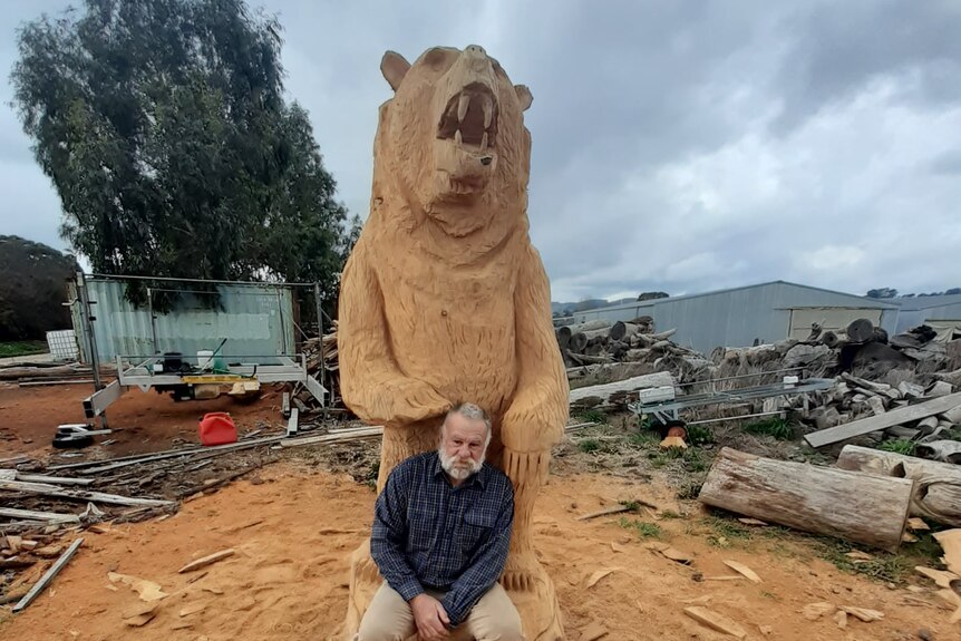 Man sitting on tree stumped carved into a gizzly bear.