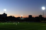 A general shot of cricketers playing under lights at sunset.