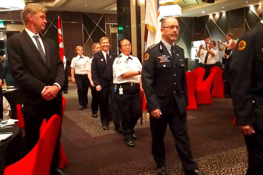 A smiling woman walks in line with others at an awards ceremony