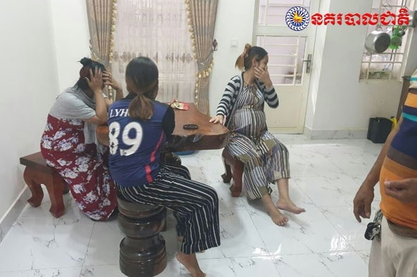 Three women, one of them heavily pregnant, cover their mouths and faces after being arrested by police in Cambodia.