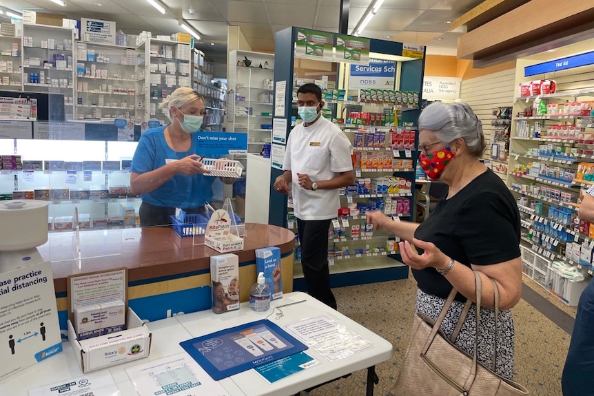 a lady is served at a pharmacy counter as a pharmacist looks on