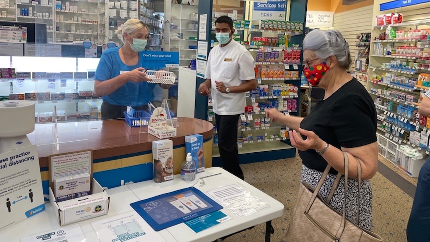 a lady is served at a pharmacy counter as a pharmacist looks on