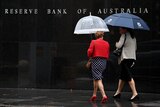 Two women with umbrellas walk past the Reserve Bank building.