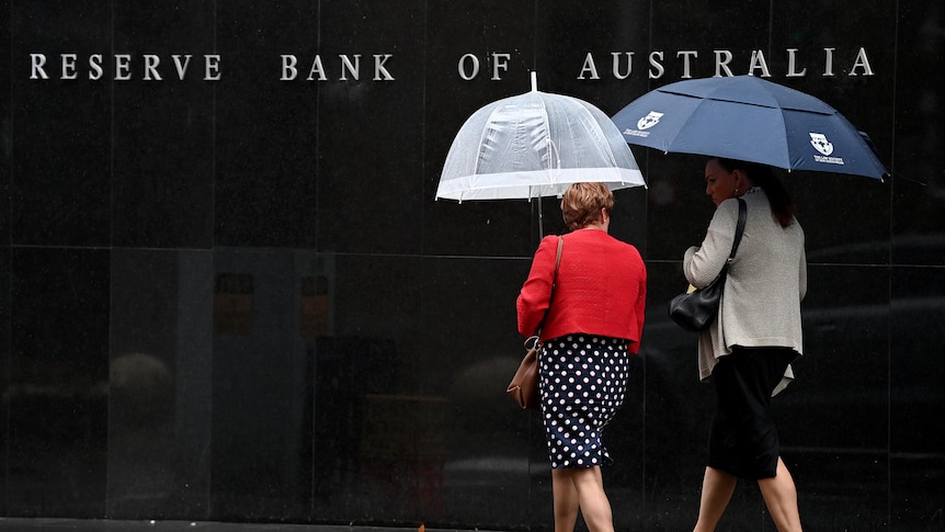 Two women with umbrellas walk past the Reserve Bank building.