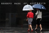 Two women with umbrellas walk past the Reserve Bank building.