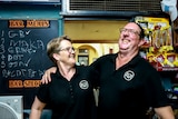 Man and woman wearing black shirts smile in front of pub bar