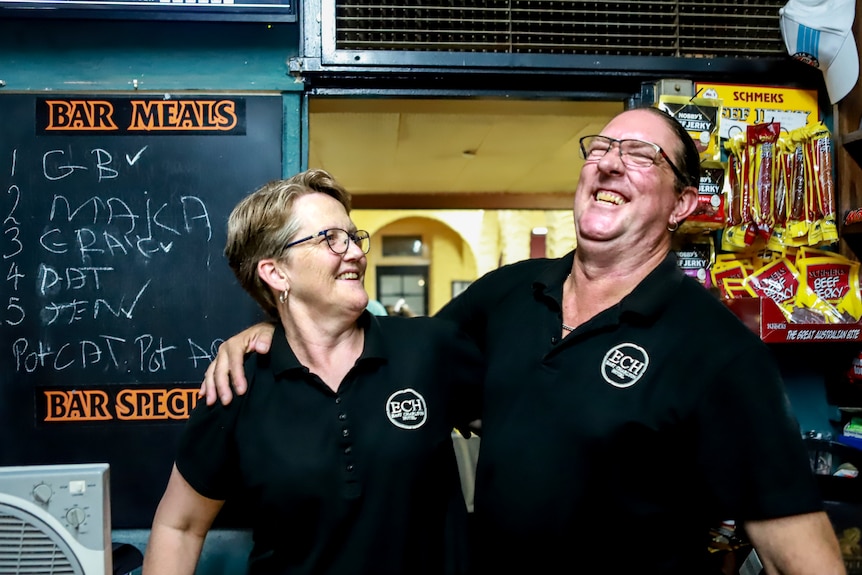 Man and woman wearing black shirts smile in front of pub bar