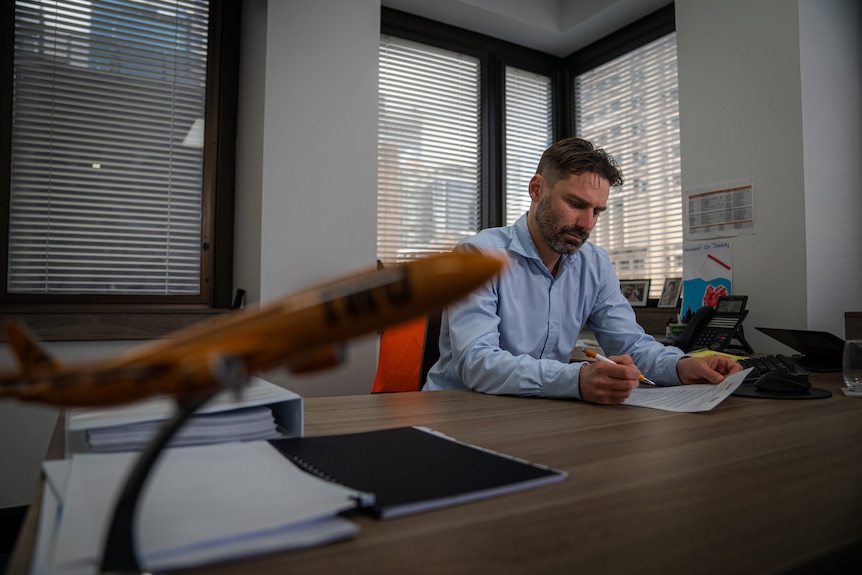 A man with a blue button up shirt looks at a desk.