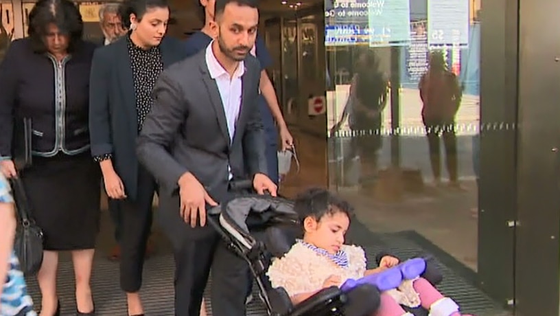 family pushing a young girl in a wheelchair out of a court