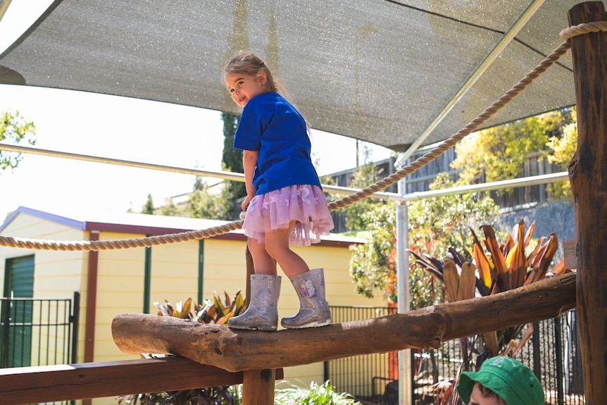 A young girl wearing gum boots balances on a beam off the ground.