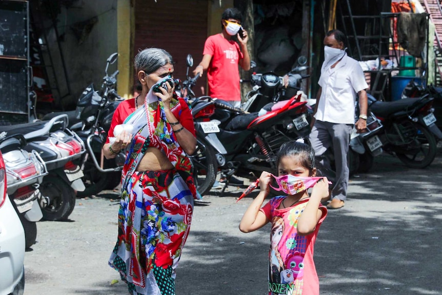 A little girl in a Frozen dress and mask walking down the street next to an older woman in a sari