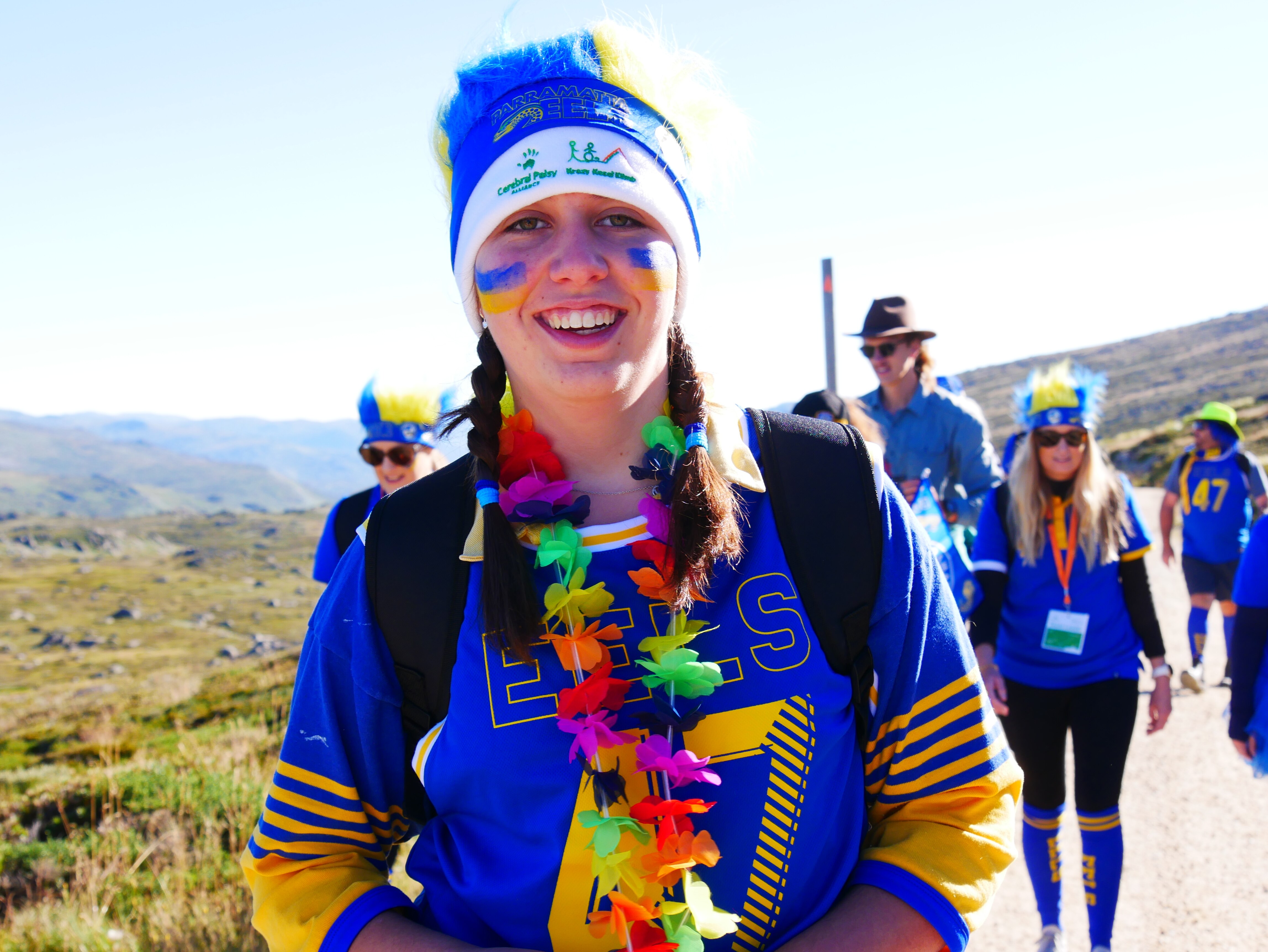a young girl smiles at the camera whilst climbing a mountain, wearing bright blue colours