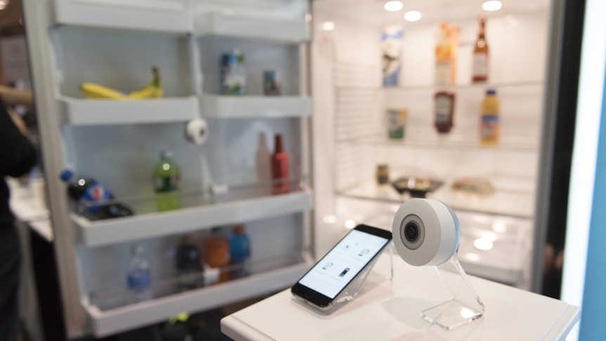 A small camera and phone in front of an open fridge door.