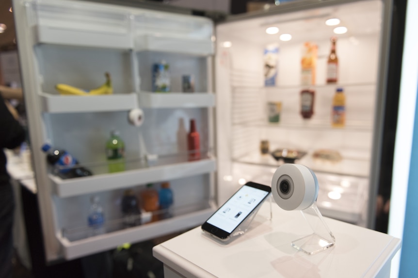 A small camera and phone in front of an open fridge door.