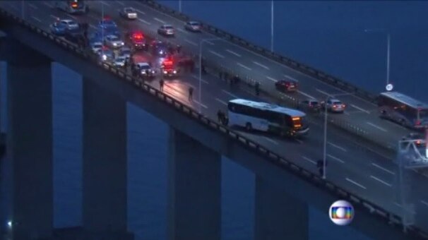 An aerial shot showing police cars surrounding a bus on a bridge above water.