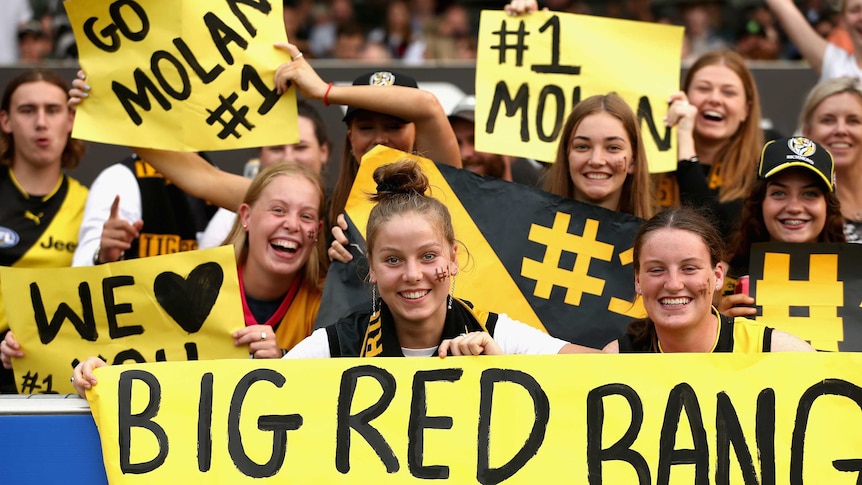 A group of teenage fans hold up black and yellow placard