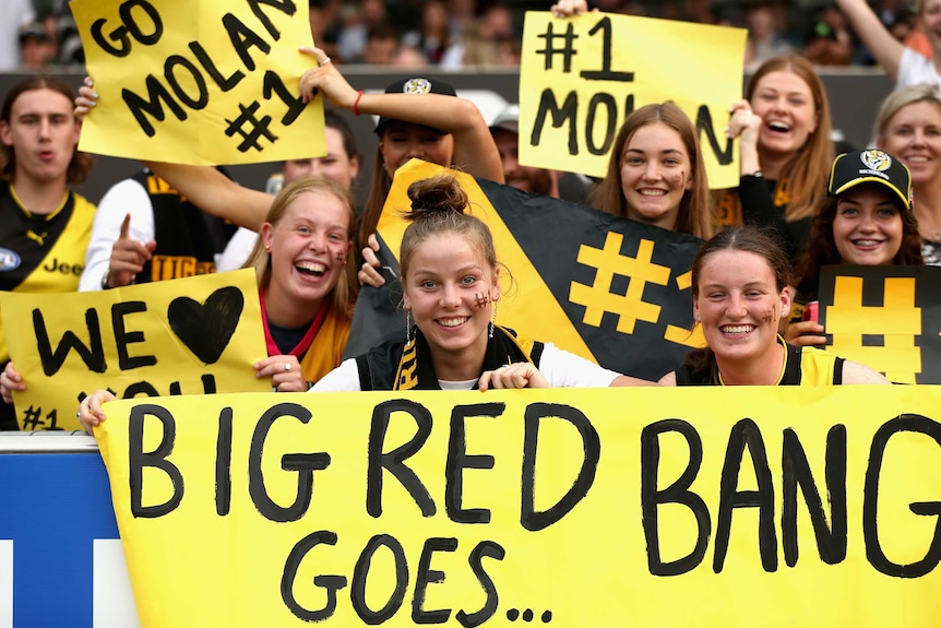 A group of teenage fans hold up black and yellow placard