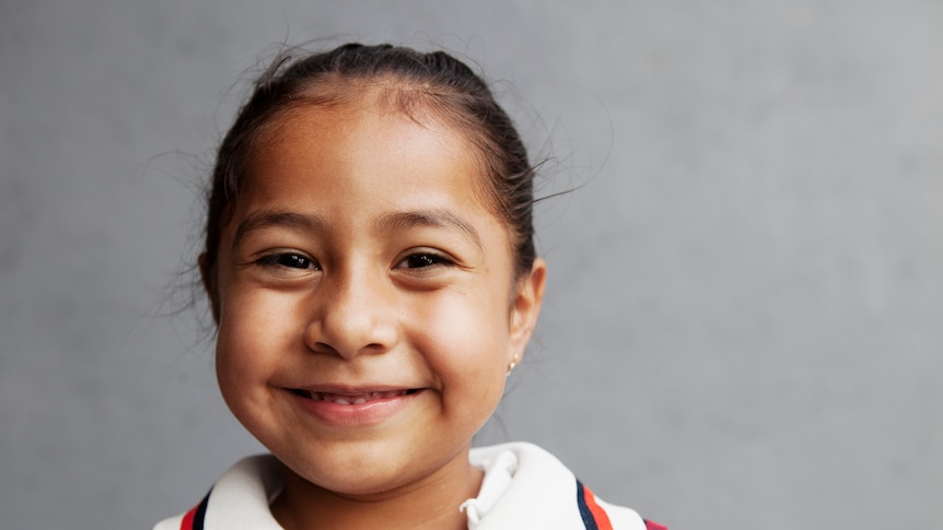 A young Mexican girl in a school uniform smiling 