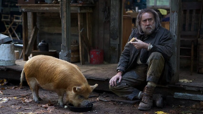 Nicholas Cage who plays Rob in the movie Pig is sitting down eating next to his pig.