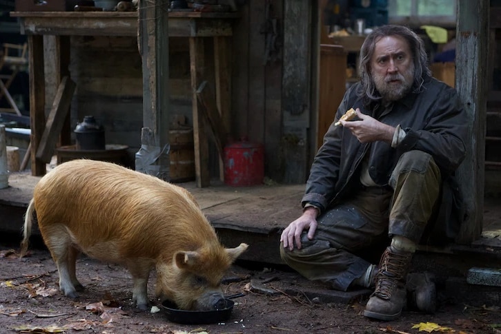 Nicholas Cage who plays Rob in the movie Pig is sitting down eating next to his pig.