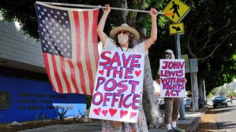 A woman waving a flag wearing a sign that says 'save the post office'