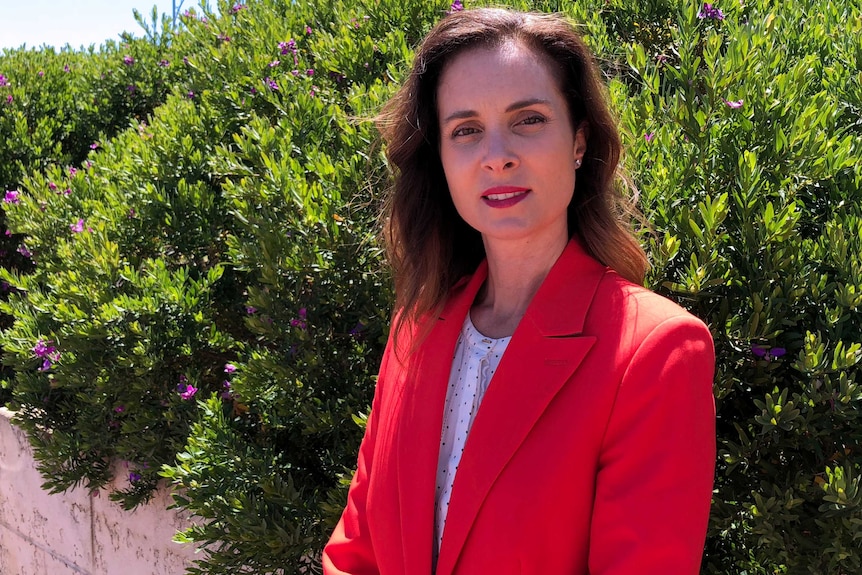 A mid shot of Louise Stewart wearing a red jacket standing in front of green bushes.