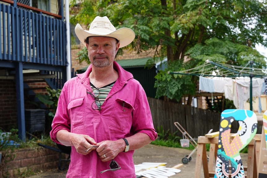 A man in a pink shirt and cowboy hat in a backyard