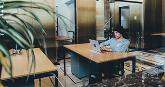 A man works on a laptop in an office filled with plants.