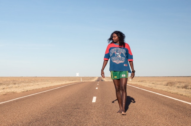 Baker Boy walks down an empty road.