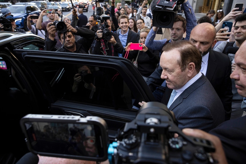 Kevin Spacey opens car door to step inside, media swarm his car with cameras. 