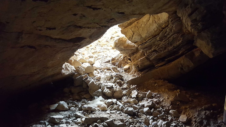 A large pile of rubble and rocks spills through the entrance of the underground cave.
