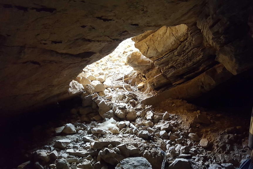 A large pile of rubble and rocks spills through the entrance of the underground cave.