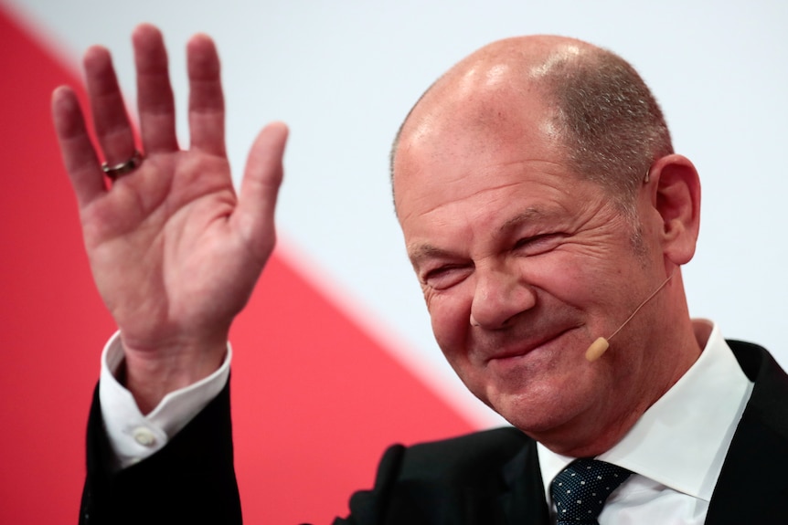 German politician Olaf Scholz waves while smiling.
