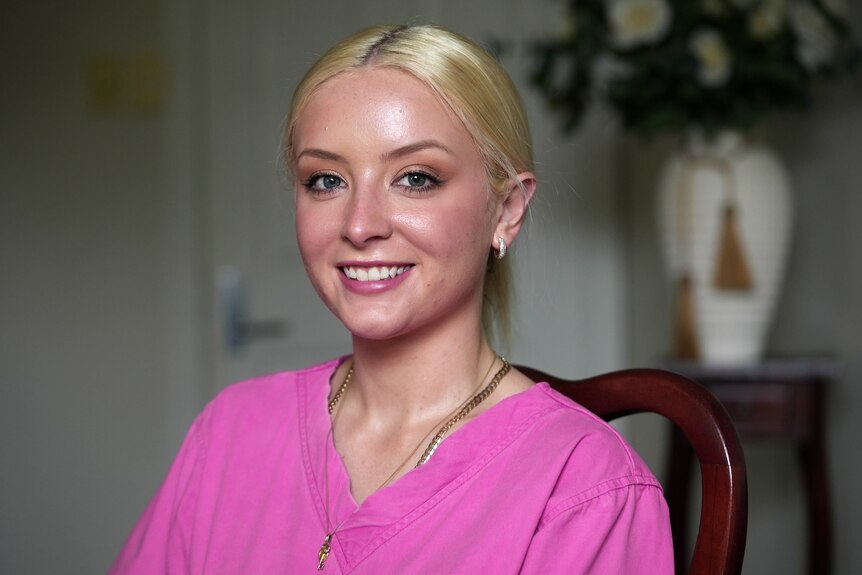 A young smiling blonde woman wearing pink scrubs.