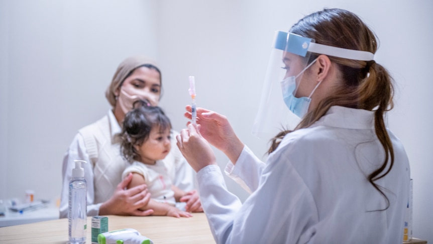 A small girl is prepped for a COVID-19 vaccination as she sits on a woman's lap.