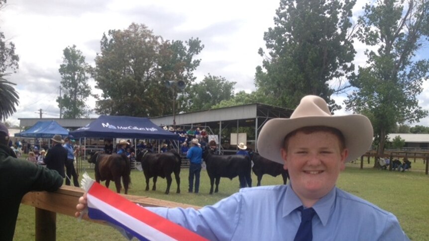 A very happy high school student holds his ribbon after winning a steer competition